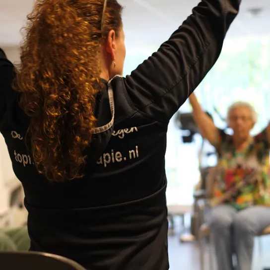 Fysiotherapeut doet oefening voor, klant doet hem na